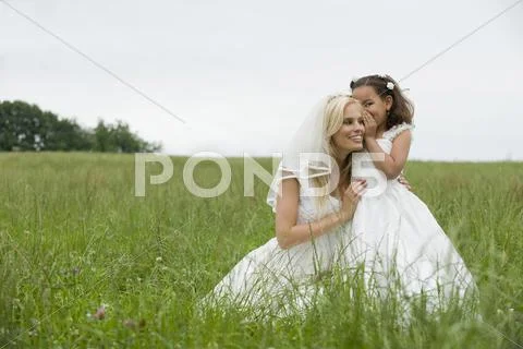Flower girl (4-5) whispering to bride on meadow Stock Photos