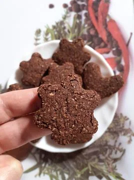 Flower shaped chocolate oat cookie, held by two fingers. Stock Photos