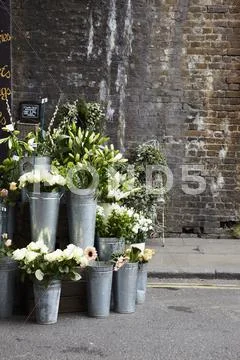 A Flower Stall With Zinc Vases In Front Of An Old Brick Wall