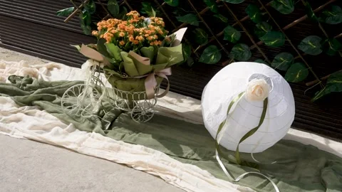 Flowers in a basket and a lantern set up next to a green cloth in a garden area Stock Footage 334979830