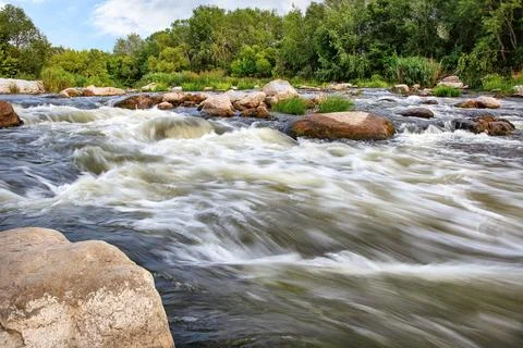 Flowing river dances over smooth stones in a serene natural landscape Stock Photos