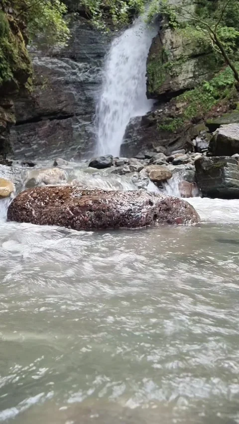 Flowing River Water Between Rocks with Blurred Waterfall Background Stock Footage 328297924