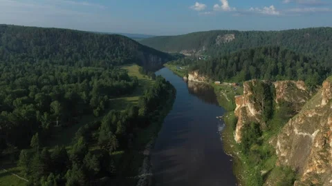 Flowing river winding through a vibrant green valley surrounded by steep cliffs Vídeo Stock 289845443