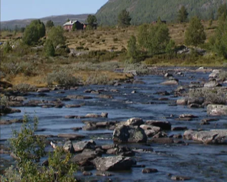 Flowing stream in tundra + log cabin in glacial landscape - Norway Stock Footage 37667723