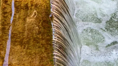 Flowing water dances over a rustic wooden edge, capturing the beauty of nature Stock Footage 331967507