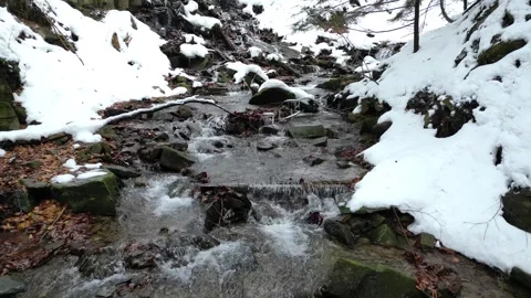 Flowing winter stream cascades down rocky terrain revealing layers of snow and Vidéo 335887327