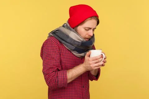 Flu-sick guy treated with warm tea, holding cup feeling unwell with sore thro Stock Photos