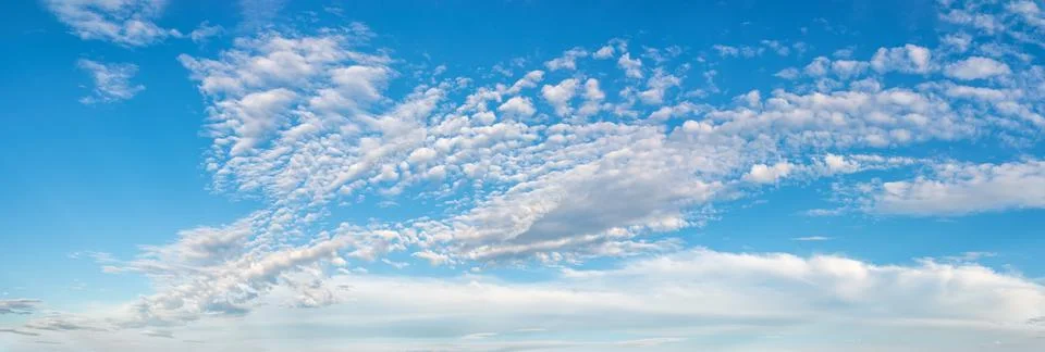 Fluffy cirrus clouds float slowly high in the azure blue sky on a sunny day. Stock Photos