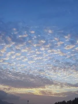 A fluffy cloud pattern covers the sky, while the horizon is illuminated Stock Photos