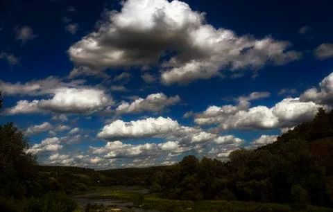 Fluffy clouds in the blue sky over the winding river Stock Photos
