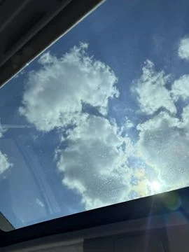 Fluffy clouds in a blue sky through blurry window, sunny weather Stock Photos