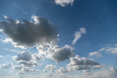 Fluffy clouds drift gracefully in a vibrant blue sky, casting gentle shadows  Stock Photos