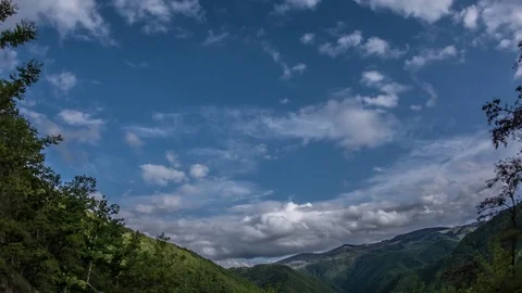 Fluffy clouds moving quickly over mountains covered with thick forests Stock Footage 69831916