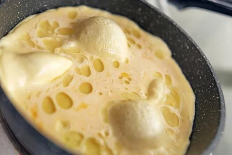 Fluffy omelet with large bubbles, fried in olive oil in a black skillet Stock Photos