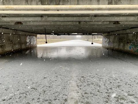 Fluffy snowflakes drift down in a tranquil setting beneath a concrete bridge. Stock Photos