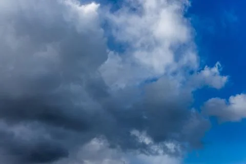 Fluffy white and grey clouds against a bright, colorful blue sky Stock Photos