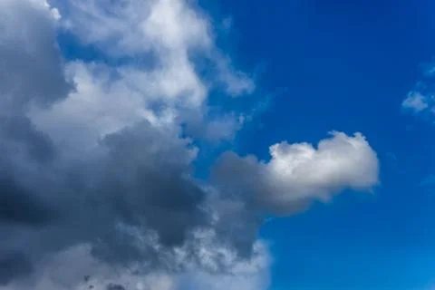 Fluffy white and grey clouds against a bright, colorful blue sky Stock Photos