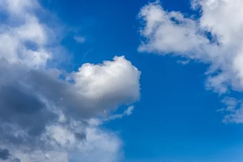 Fluffy white and grey clouds against a bright, colorful blue sky Stock Photos