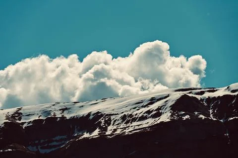 Fluffy White Cloud Resting Above a Snow-Dusted Mountain Ridge Stock Photos
