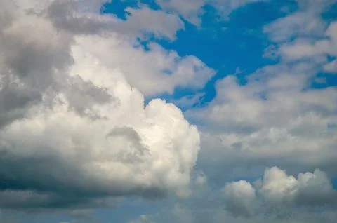 Fluffy white clouds against a bright blue sky with sections of gray Stock-Fotos