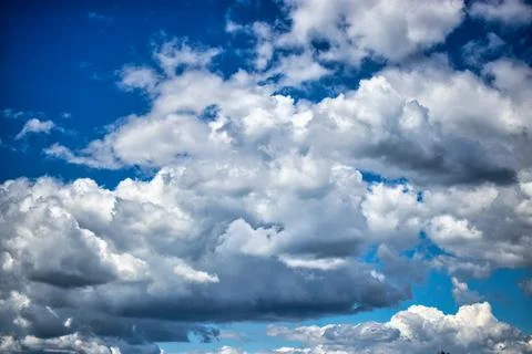Fluffy white clouds dance across the bright blue sky, casting playful shadows Stock Photos