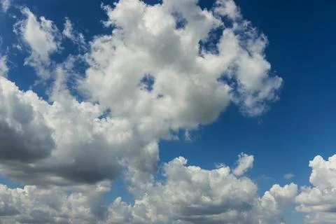 Fluffy white clouds dominate bright blue sky during sunny afternoon Stock Photos