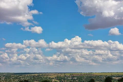Fluffy white clouds drift across a vivid blue sky, casting playful shadows on Stock Photos