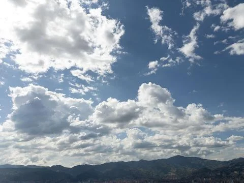 Fluffy white clouds drift across a vibrant blue sky, mountains in the distanc Stock Photos