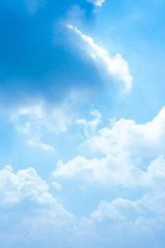Fluffy white clouds float across a bright blue sky during a sunny summer day Stock Photos