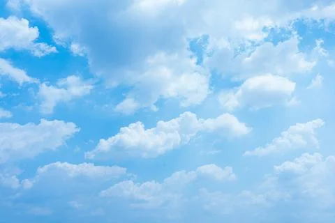 Fluffy white clouds float across a bright and clear sunny blue summer sky Stock Photos