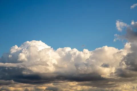 Fluffy white clouds float gracefully in a blue sky during at sunset Stock Photos