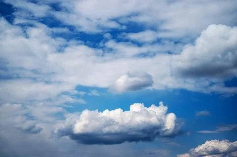 Fluffy white clouds floating across deep blue sky Stock Photos
