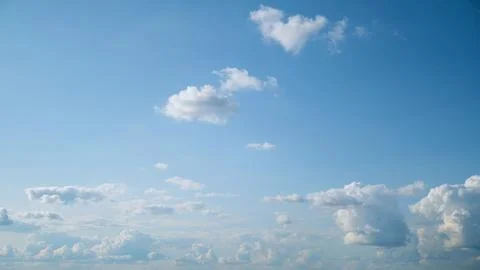 Fluffy white clouds gracefully drift across the daytime blue sky, creating a 写真素材