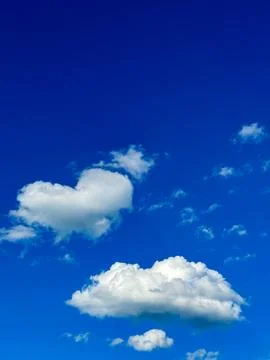 Fluffy White Clouds With One Shaped Like a Heart Floating in a Vast Blue Sky Stock Photos