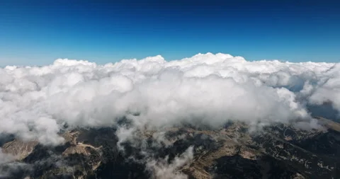 Fluffy white clouds roll over jagged mountain peaks Stock Footage 303317807