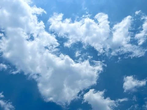 Fluffy white clouds scattered across a vibrant blue sky on a bright sunny day Stock Photos
