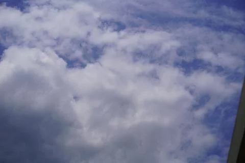 Fluffy white cumulus clouds drifting across a bright blue summer sky background Stock Photos