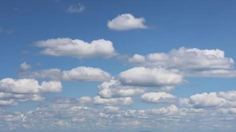 Fluffy white cumulus clouds float against a bright blue sky. Stock Photos