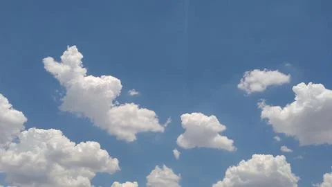 Fluffy white cumulus clouds floating across a bright blue sky Stock Photos