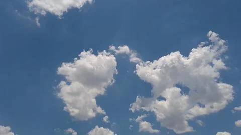 Fluffy white cumulus clouds floating across a bright blue sky Stock Photos