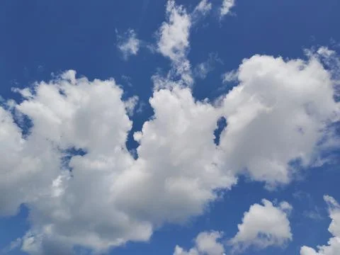 Fluffy white cumulus clouds scattered across vibrant blue sky on a sunny day. Stock Photos