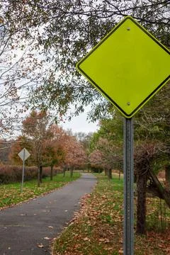 Fluorescent green triangular yield sign near a country walking path near tree Stock Photos