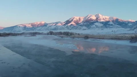 Fly along freezing river with mountain glowing in sunset light Stock Footage 310529146