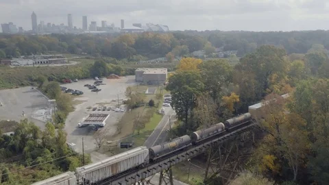 Fly along moving train over railroad bridge to tilt up to Atlanta skyline Stock Footage 82448309