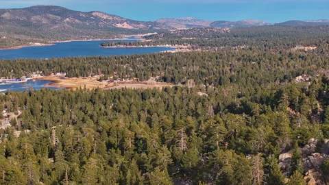 Fly around mountain peak amid pine forest reveal lake and mountains Stock Footage 329910059