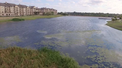 Fly Low Over Grass Over Water By Lakeside Apartment Complex Stock Footage 76381447