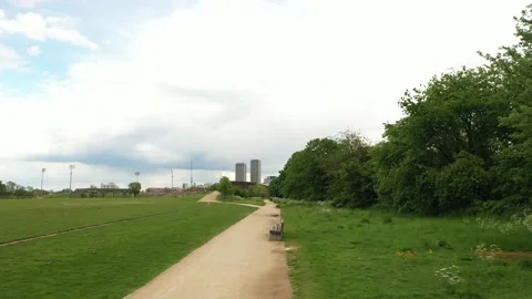 Fly from meadow over path to strip of trees and shrubs on edge of park Stock Footage 155849138
