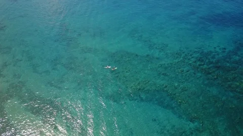 Fly over blue surface of ocean with two indigenous people which swimming on surf Stock Footage 100517945