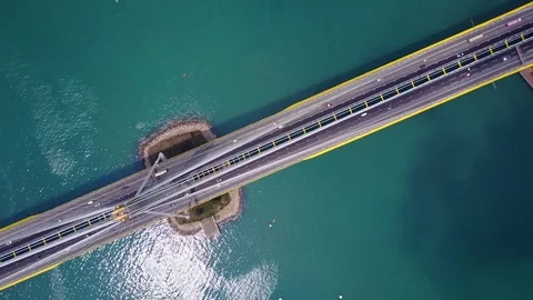 Fly over large modern bridge, blue green channel waters under, small traffic Stock Footage 75990791