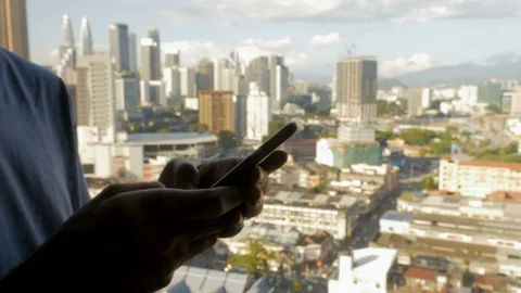 Fly over a man typing on his cell phone overlooking a modern city Stock Footage 86660784